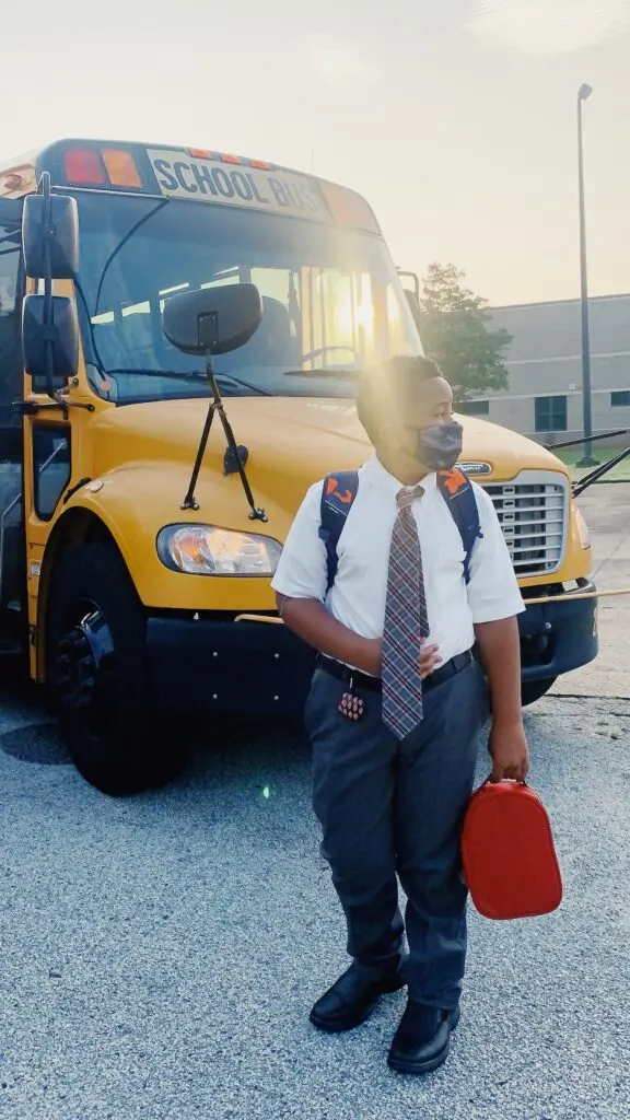 kid standing in front of school bus in mask . 