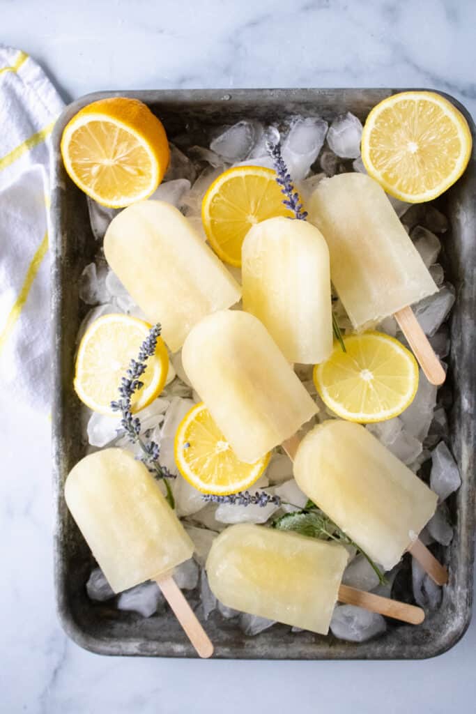 Lavender lemonade Popsicles on a tray with lemons and lavender sprigs